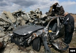 Пожилой японец молится о погибшем сыне у остова автомашины, в которой тот погиб во время цунами